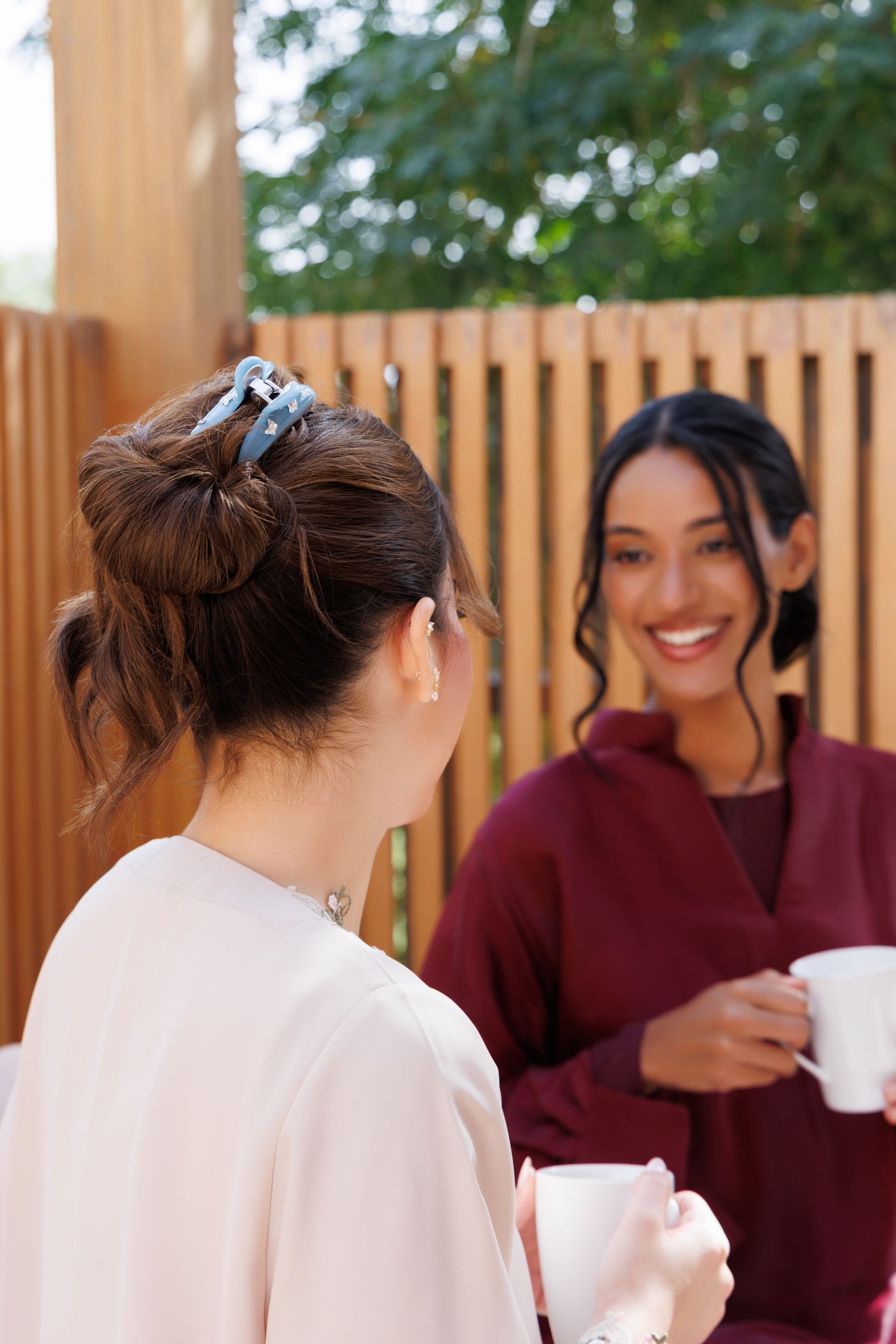 Two friends laughing over tea, one wearing a blue Alexandre de Paris claw clip
